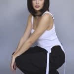 Woman with sleek, dark bob wig in casual outfit against gray background.
